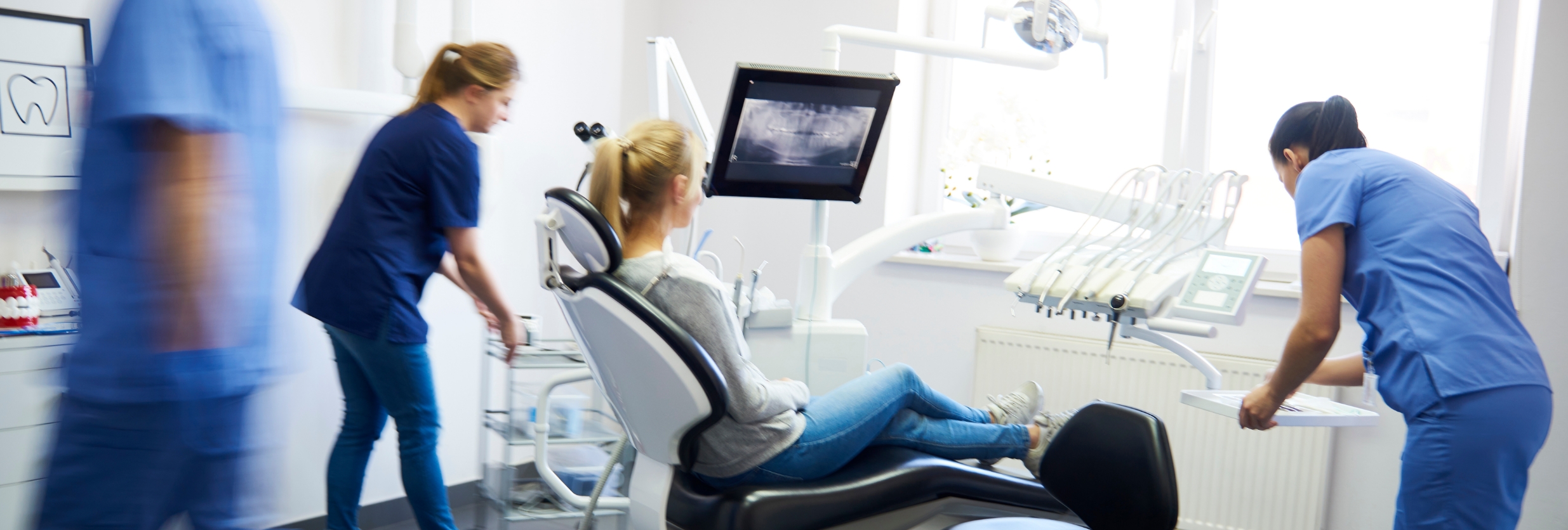 three dentists around a patient in a dental chair all looking at an xray image